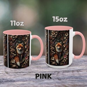 Op de afbeelding: Twee roze en witte keramische mokken met een vos-illustratie. De mokken zijn verkrijgbaar in 11oz en 15oz formaten. De vos is omringd door bloemen en bladeren.