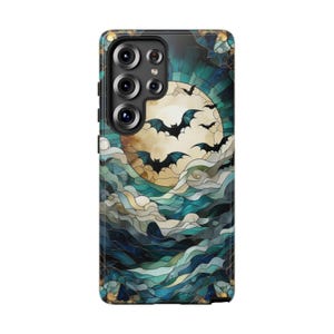 May include: A phone case featuring a stained-glass design with a full moon, bats, and swirling clouds in shades of blue, teal, and gold. The case has a black camera module with multiple lenses.