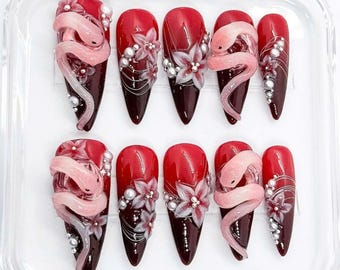 May include: Set of ten red and black ombre press-on nails with a pink snake and white flower design.