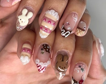 May include: Close-up of a hand with several nails painted with different designs. The nails feature a variety of cute designs, including ice cream cones, bunnies, and cherries. The nails are painted in shades of pink, white, brown, and yellow.