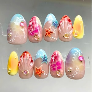 May include: Ten oval-shaped false nails with a summer beach theme. The nails are painted with a light blue, pink, and yellow gradient. Each nail features a different design, including seashells, starfish, and a blue fish.