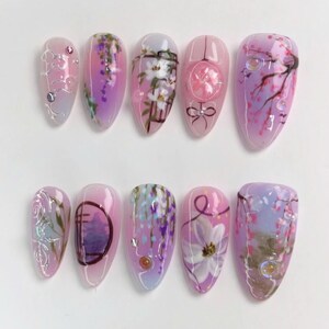 May include: Set of ten pink and purple false nails with floral designs. The designs include wisteria, cherry blossoms, and a traditional Japanese gate.