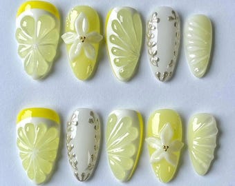 Puede incluir: Conjunto de diez uñas postizas amarillas y blancas con varios diseños, incluyendo limones, flores y remolinos.