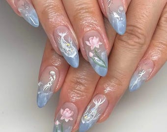 May include: Close-up of a hand with light blue almond-shaped nails featuring a gradient design with white floral and fish illustrations.