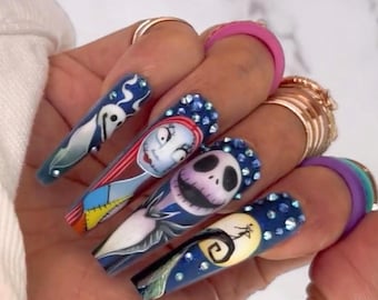 Puede incluir: Uñas acrílicas largas, puntiagudas, azules, blancas y rojas con temática de Pesadilla antes de Navidad. Las uñas están decoradas con pedrería y presentan imágenes de Jack Skellington, Sally y el fantasma de la película.