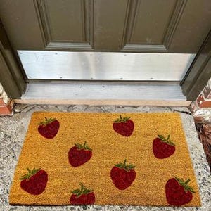 May include: A brown coir doormat with a pattern of red strawberries. The doormat is rectangular and has a textured surface.