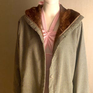 May include: A black and white checkered coat with a brown faux fur-lined hood. The coat is open, revealing a pink halter top. The coat has a single button closure.