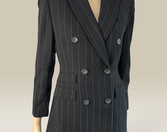 May include: A black double-breasted blazer featuring thin white pinstripes, a notched lapel, and six dark buttons arranged in two vertical rows. The jacket includes two flap pockets at the waist and long sleeves, displayed on a mannequin.