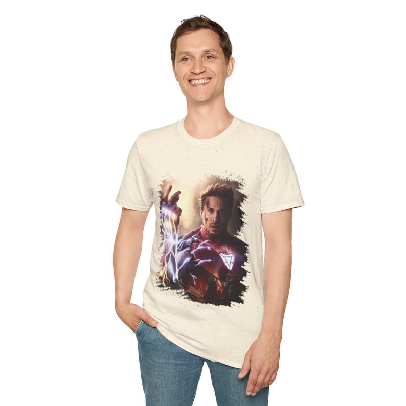 May include: A beige t-shirt with a graphic print of Iron Man in his red and gold suit, with a blue and purple energy effect around his arm. The graphic is set against a black and white background.