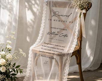 May include: A wooden chair draped with a sheer white fabric runner, edged with lace. The runner has the words "Reserved In Memory Of" and a name, plus a poem. A bouquet of white flowers is tied to the chair.