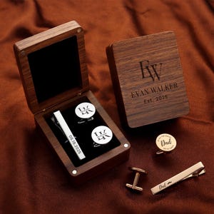 May include: A wooden box set with personalized cufflinks, tie clip, and a box lid engraved with initials and the name "Evan Walker". The set includes a gold-coloured tie clip with the word "Dad" and a moustache design.