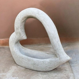 May include: A gray concrete heart-shaped planter with a smooth, slightly textured surface. The planter is designed to hold small plants or flowers.