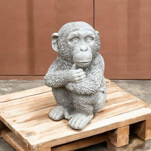 May include: A gray concrete statue of a monkey sitting with its arms crossed and looking to the side.