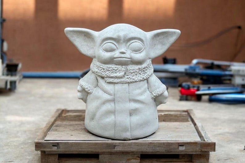 K&ouml;nnte beinhalten: Eine wei&szlig;e Betonstatue eines fiktiven Charakters mit gro&szlig;en Ohren, einem Pelzkragen und einem Mantel. Die Statue steht auf einer Holzplattform.