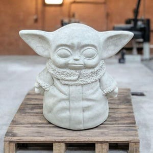 K&ouml;nnte beinhalten: Eine wei&szlig;e Keramikstatue eines fiktiven Charakters mit gro&szlig;en Ohren und einem Pelzkragen. Die Statue steht auf einer Holzplattform.