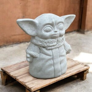 K&ouml;nnte beinhalten: Eine graue Betonstatue einer fiktiven Figur aus dem Star Wars-Franchise. Die Figur tr&auml;gt einen Pelzmantel und hat gro&szlig;e Ohren.