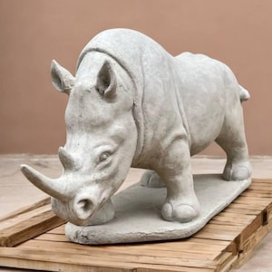 May include: A white concrete sculpture of a rhinoceros standing on a wooden platform.