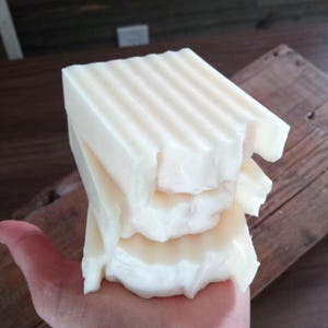 May include: A stack of three white soap bars with a rippled texture. The top bar has a slightly chipped edge.