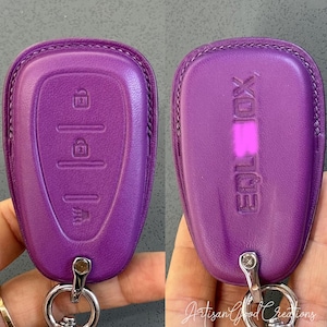May include: A pair of purple leather key fob covers. One cover displays key function symbols, the other has the word "EQLIOX" embossed. Both have a silver key ring attached.