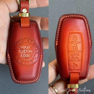 Może przedstawiać: Spersonalizowany skórzany brelok do kluczy w kolorze czerwonobrązowym. Posiada okrągły emblemat z napisem "YOUR CUSTOM LOGO" i "UNITED STATES". Tył pokazuje funkcje klawiszy. Przymocowany do skórzanego paska i złotego osprzętu. Ma około 10 cm długości.