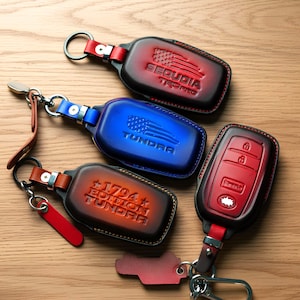 May include: Leather key fob covers in red, blue, and brown with silver key rings. The red cover has the text "SEQUOIA TRD PRO" and an American flag design. The blue cover says "TUNDRA" with an American flag. The brown cover says "1794 EDITION TUNDRA".