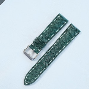 May include: A two-piece watch strap in a deep forest green color with a textured, pebbled surface. The strap features contrasting white stitching along the edges and includes a polished silver-tone metal buckle attached to one of the two pieces.