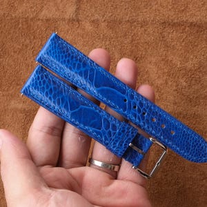 May include: Vibrant blue watch straps with a textured pattern and a silver buckle. The straps are displayed against a brown backdrop. The watch straps are a striking blue colour.