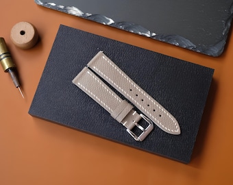 Peut inclure: Un bracelet de montre taupe en deux parties avec une surface texturée, des surpiqûres blanches contrastantes sur les bords et une boucle en métal argenté poli. Le bracelet se compose de deux pièces distinctes, une avec boucle et une perforée.
