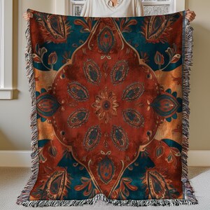 May include: A woven throw blanket with a colorful paisley pattern in shades of red, orange, teal, and brown. The blanket has a fringed edge.