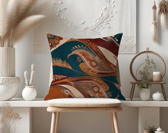 May include: A decorative throw pillow with a paisley pattern in shades of brown, red, teal, and cream. The pillow is sitting on a wooden chair in a room with a white wall and a vase of dried pampas grass.