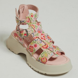 May include: Pink platform sandals with a floral print and multiple straps. The sandals have a chunky platform sole and a buckle closure.