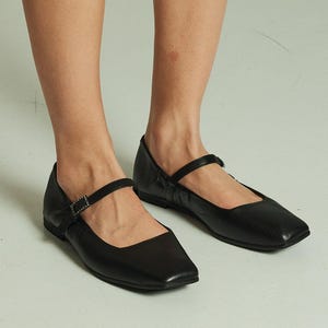 Può includere: Ballerine nere in pelle con punta quadrata e cinturino con fibbia. Le scarpe hanno un tacco basso e sono realizzate in pelle morbida e flessibile.