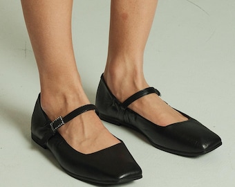 Op de afbeelding: Zwarte leren ballerina's met vierkante neus en een gespsluiting. De schoenen hebben een lage hak en zijn gemaakt van zacht, soepel leer.
