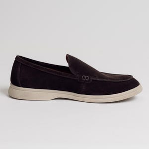 Op de afbeelding: Een donkerbruine su&egrave;de loafer met een ronde neus en een lichtbeige zool. De schoen heeft een klassiek instapontwerp, geschikt voor casual of semi-formele gelegenheden.