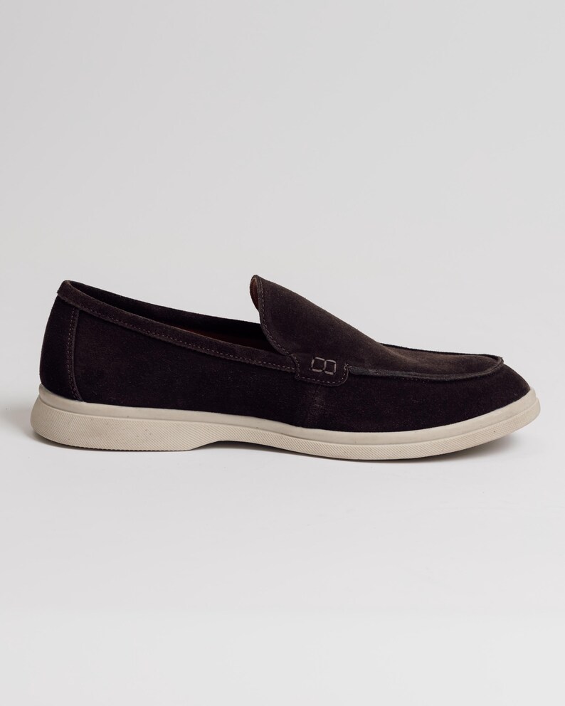 Op de afbeelding: Een donkerbruine su&egrave;de loafer met een ronde neus en een lichtbeige zool. De schoen heeft een klassiek instapontwerp, geschikt voor casual of semi-formele gelegenheden.