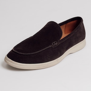 Op de afbeelding: Een donkerbruine su&egrave;de loafer met een cr&egrave;mekleurige zool. De schoen heeft een klassiek instapontwerp met een gestikt detail op de wreef. De binnenvoering is lichtbruin.