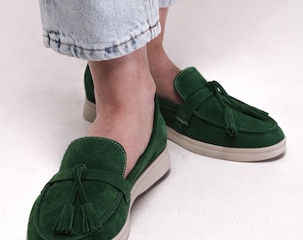 May include: A pair of green suede loafers with a tassel detail. The loafers have a white rubber sole and are worn with light blue jeans.