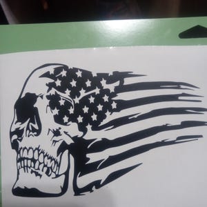May include: A black and white skull decal with an American flag design. The flag is tattered and flowing in the wind. The skull is facing left and has a detailed design.