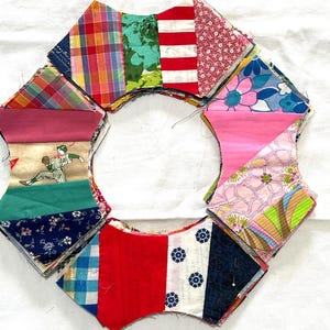 May include: A circular arrangement of fabric scraps featuring diverse patterns including a baseball player graphic, red and white stripes, floral prints, plaid, and solid colors. The pieces are layered and stitched together in a star-like shape.