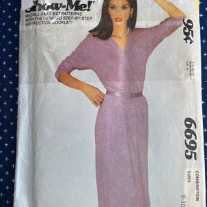 May include: A McCall's Show-Me sewing pattern envelope for a dress, number 6695, featuring a photograph of a lavender-colored dress with long sleeves, a collared neckline, and a matching belt. The envelope includes text detailing the pattern.