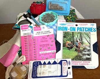 May include: A collection of sewing supplies including safety pins, needles, hooks, snaps, iron-on patches, and thread. The image features various packages and containers with sewing notions, perfect for crafting and mending projects.