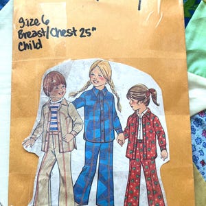 May include: A vintage sewing pattern envelope from Simplicity, featuring a child's clothing design. The envelope is tan with handwritten text indicating size 6, a 25-inch chest, and the word "Child". The illustration shows three children in matching outfits.