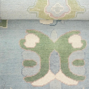 Op de afbeelding: Een lichtblauw tapijt met een wit en groen bloemenpatroon. Het tapijt heeft een subtiele textuur en een zachte, verbleekte uitstraling.