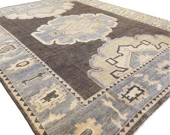 Puede incluir: Una alfombra vintage con fondo marrón y un diseño central en tonos azules y beige. La alfombra tiene un patrón geométrico con un borde de triángulos y rombos.