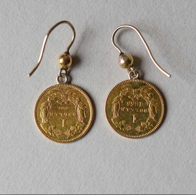 K&ouml;nnte beinhalten: Ein Paar goldene M&uuml;nzenohrringe mit einem silbernen Haken und einer goldenen Perle. Die M&uuml;nzen zeigen ein Design mit dem Jahr 1883 und dem Buchstaben F.