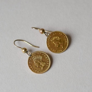 K&ouml;nnte beinhalten: Ein Paar goldene M&uuml;nzenohrringe mit einem silbernen Haken und einer goldenen Perle. Die M&uuml;nzen zeigen das Profil einer Frau mit einer Krone.