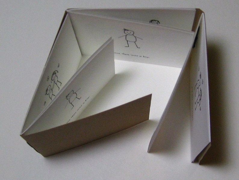 May include: A brown paper book with white pages. The book is folded into a series of triangles. The pages are decorated with simple black line drawings of stick figures.