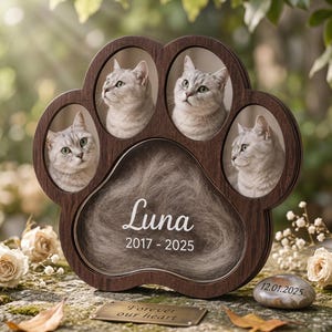 May include: A dark wood paw-shaped memorial frame featuring four oval photo slots containing images of a silver cat. The central section holds a tuft of fur with the white text Luna 2017 - 2025. A small metal plaque reads Forever our heart and a stone reads 12.01.2025.