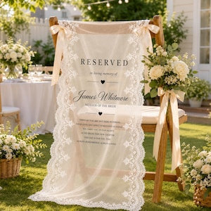 Może przedstawiać: Drewniane krzesło przykryte przezroczystym białym bieżnikiem z koronki z napisem RESERVED in loving memory of James Whitmore MOTHER OF THE BRIDE. Bieżnik jest ozdobiony kremowymi satynowymi wstążkami zawiązanymi na górnych rogach oparcia.