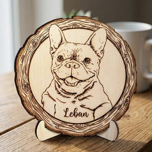 May include: A wooden plaque featuring a detailed engraving of a French Bulldog. The dog's portrait is centered within a circular frame resembling a tree cross-section. The dog's name, "Leban," is inscribed below the image. The plaque is supported by a wooden stand.